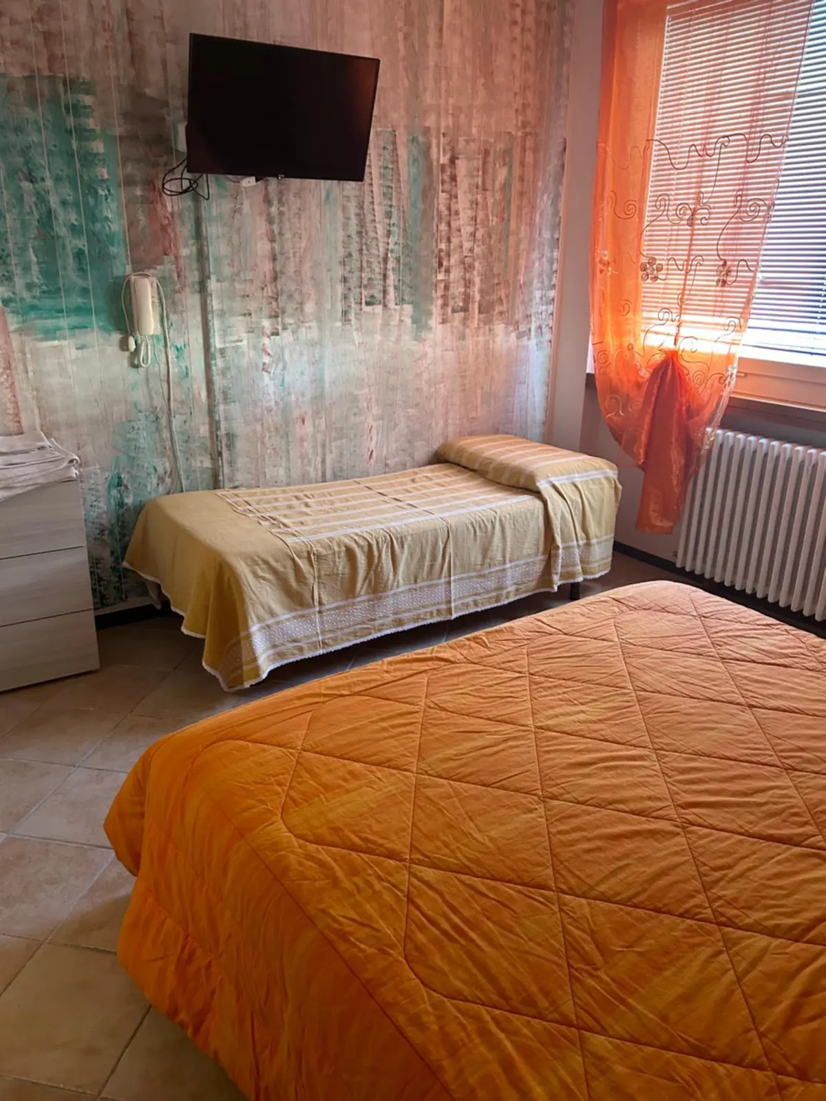 Camera tripla con il copriletto arancio e la parete decorata