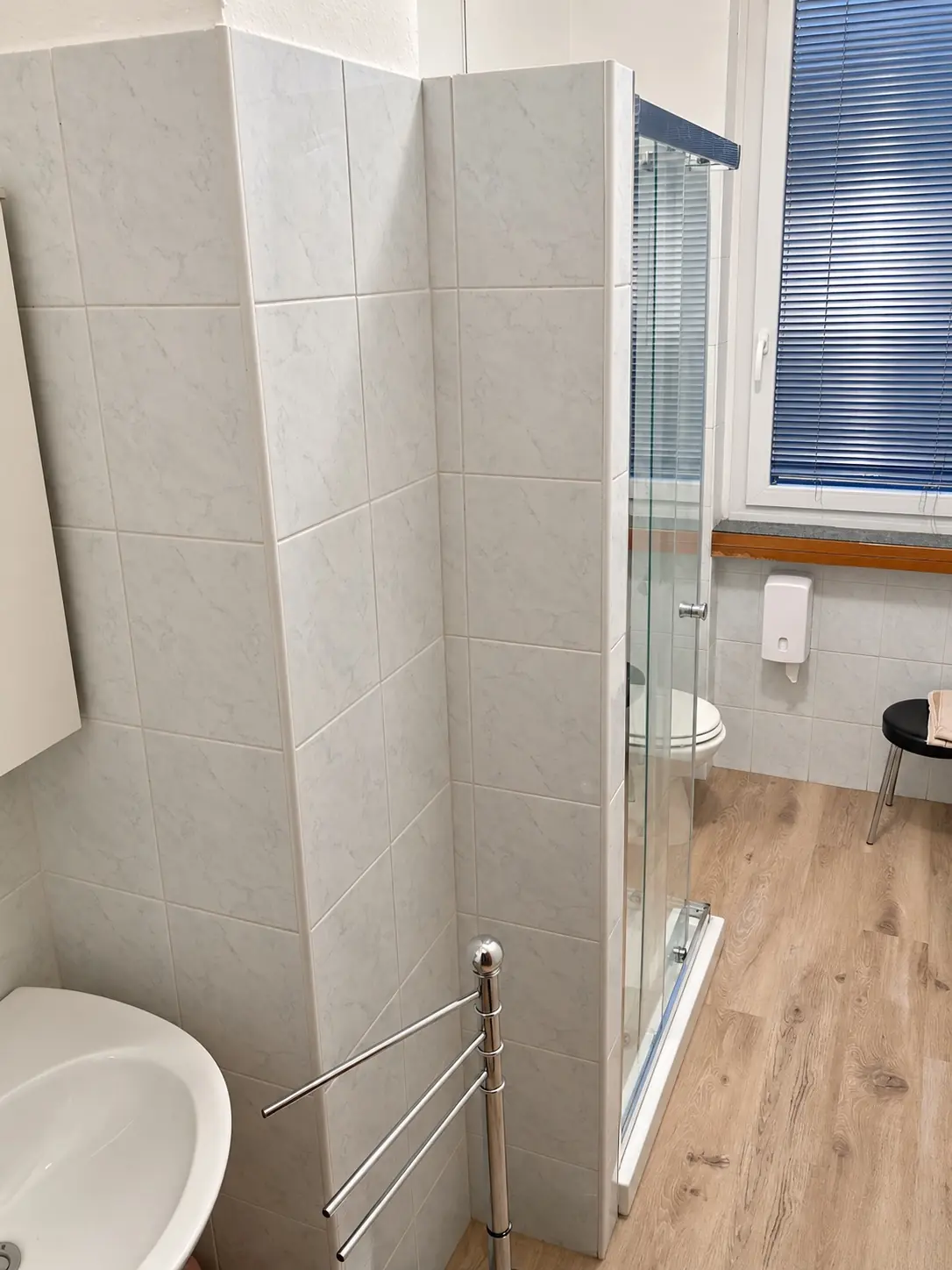Bagno di una camera, con la doccia in vetro e il pavimento effetto legno