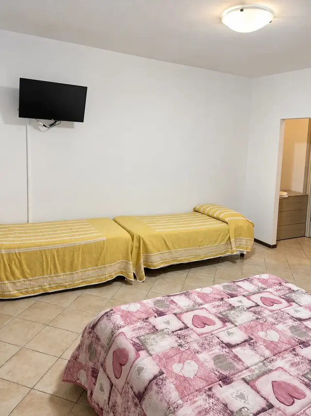 Camera tripla col letto matrimoniale rosa e due letti singoli gialli