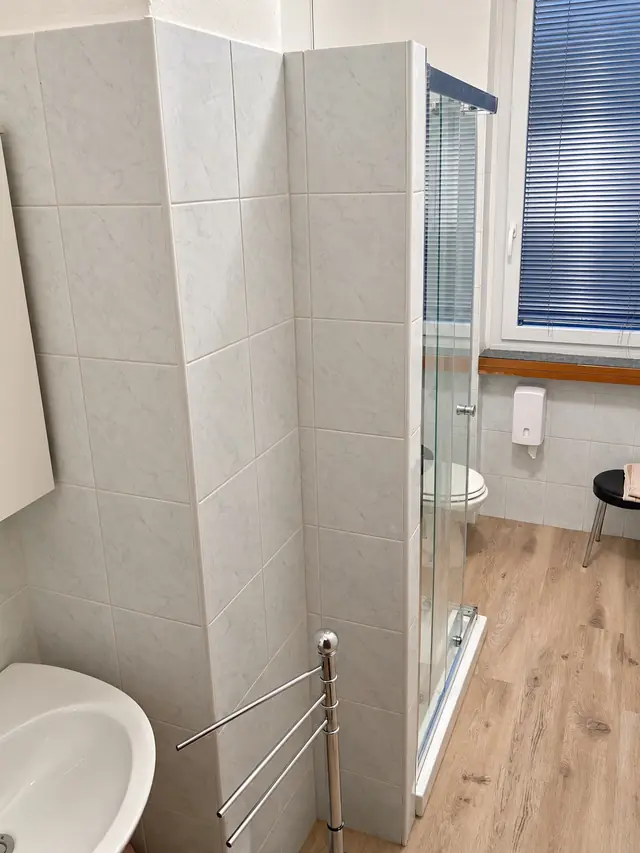 Bagno di una camera, con la doccia in vetro e il pavimento effetto legno