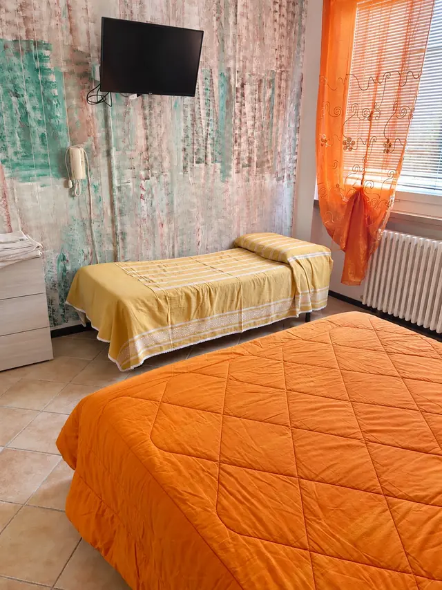 Camera tripla con il copriletto arancio, la parete decorata e le tende arancio